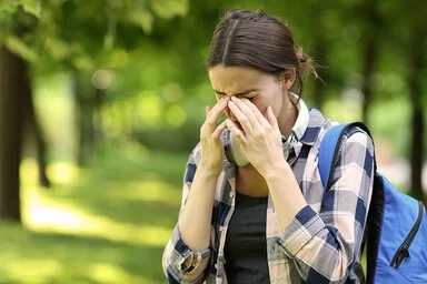 Eine junge Frau ist im Park unterwegs. Sie leidet an Allergiesymptomen und reibt sich die Augen.