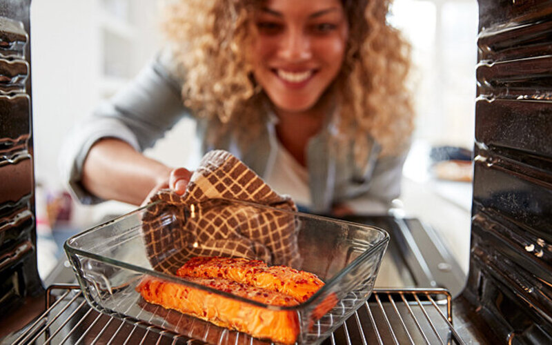 Eine Frau nimmt eine Auflaufschale mit gesundem Fisch aus dem Ofen.