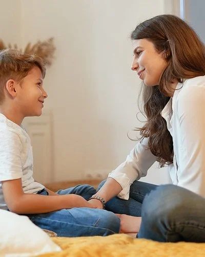 Eine junge Frau und ein junges Kind sitzen sich im Schneidersitz gegenüber und lächeln sich an.