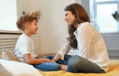 Eine junge Frau und ein junges Kind sitzen sich im Schneidersitz gegenüber und lächeln sich an.