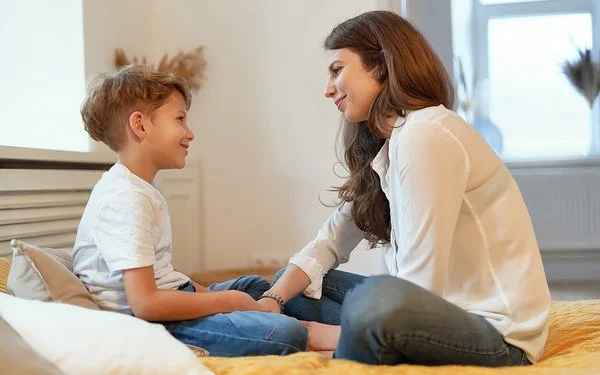 Eine junge Frau und ein junges Kind sitzen sich im Schneidersitz gegenüber und lächeln sich an.