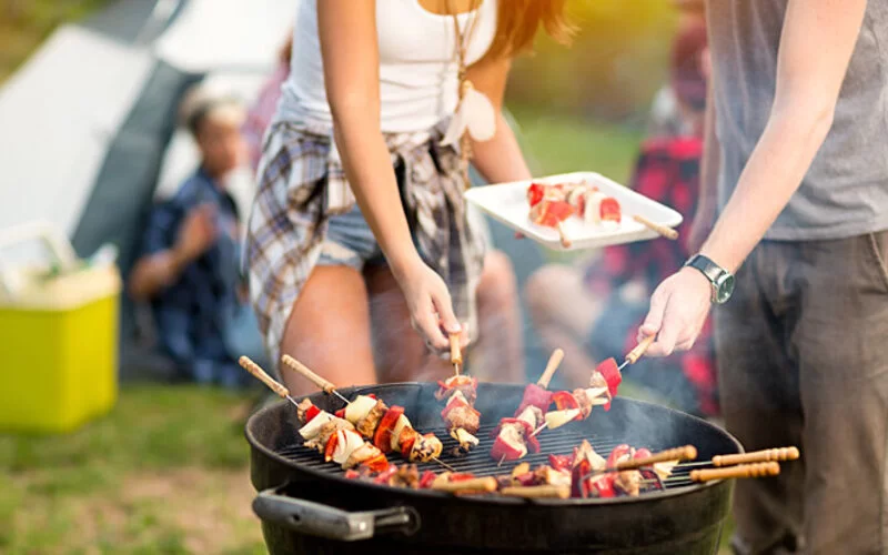 Zwei junge Leute nehmen sich Gemüsespieße von einem Grill und legen sie auf einen Teller.