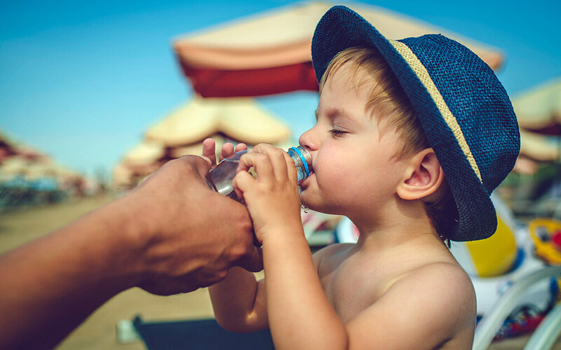 Ein Kind trinkt am Strand Wasser aus einer Flasche.