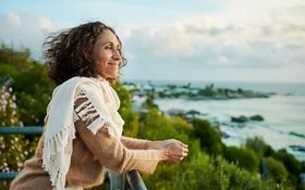 Eine Frau auf einem Balkon. Sie blickt entspannt aufs Meer.