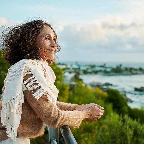 Eine Frau auf einem Balkon. Sie blickt entspannt aufs Meer.