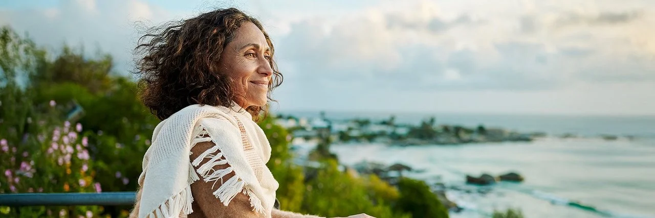 Eine Frau auf einem Balkon. Sie blickt entspannt aufs Meer.