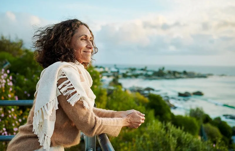 Eine Frau auf einem Balkon. Sie blickt entspannt aufs Meer.