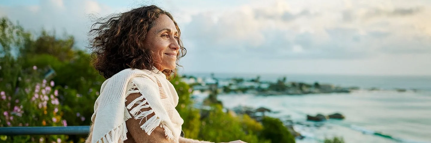 Eine Frau auf einem Balkon. Sie blickt entspannt aufs Meer.