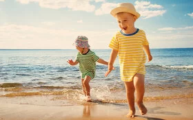 Zwei Kinder mit Sommerbekleidung toben am Strand