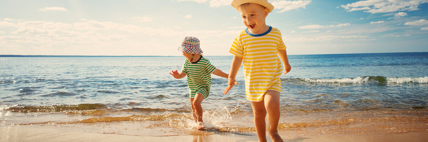 Zwei Kinder mit Sommerbekleidung toben am Strand