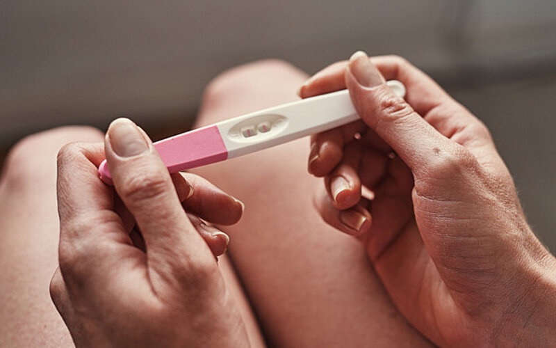 Die Hände einer Frau halten einen Schwangerschaftstest, das Ergebnisfeld zeigt zwei Striche.