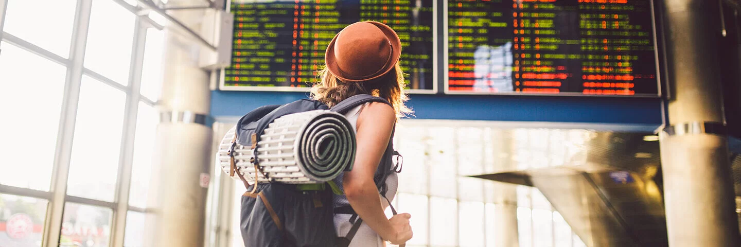 Frau schaut auf eine Anzeige am Flughafen, sie ist alleine auf einer Reise unterwegs.