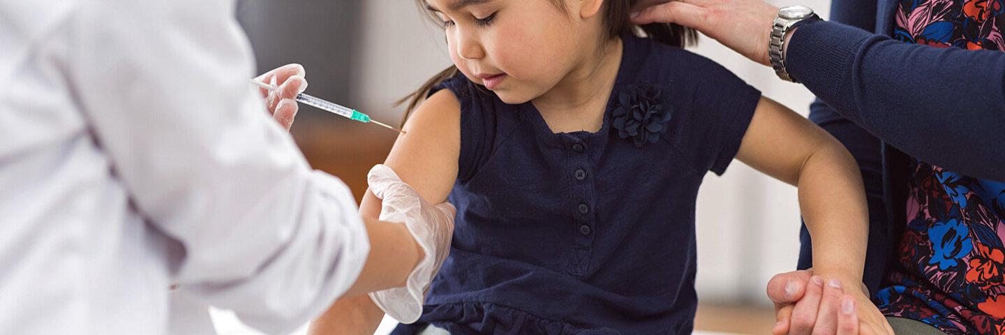 Ein Arzt verabreicht einem Mädchen eine Impfung, in Anwesenheit der Mutter.