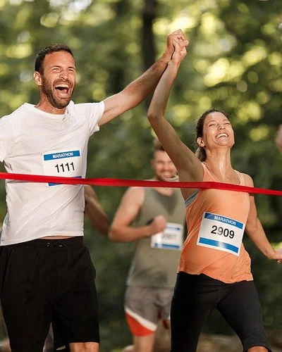 Ein junges Paar jubelt gemeinsam, während es das Band am Ziel eines Marathon-Laufs erreicht.
