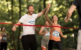 Ein junges Paar jubelt gemeinsam, während es das Band am Ziel eines Marathon-Laufs erreicht.