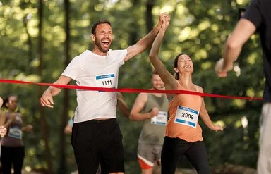 Ein junges Paar jubelt gemeinsam, während es das Band am Ziel eines Marathon-Laufs erreicht.