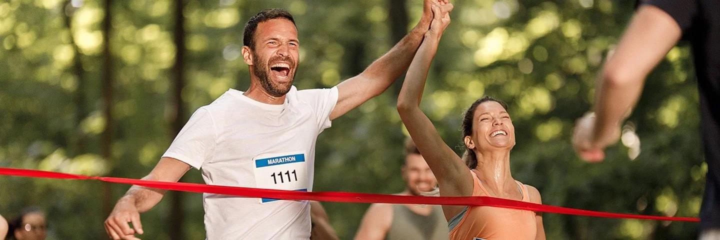 Ein junges Paar jubelt gemeinsam, während es das Band am Ziel eines Marathon-Laufs erreicht.