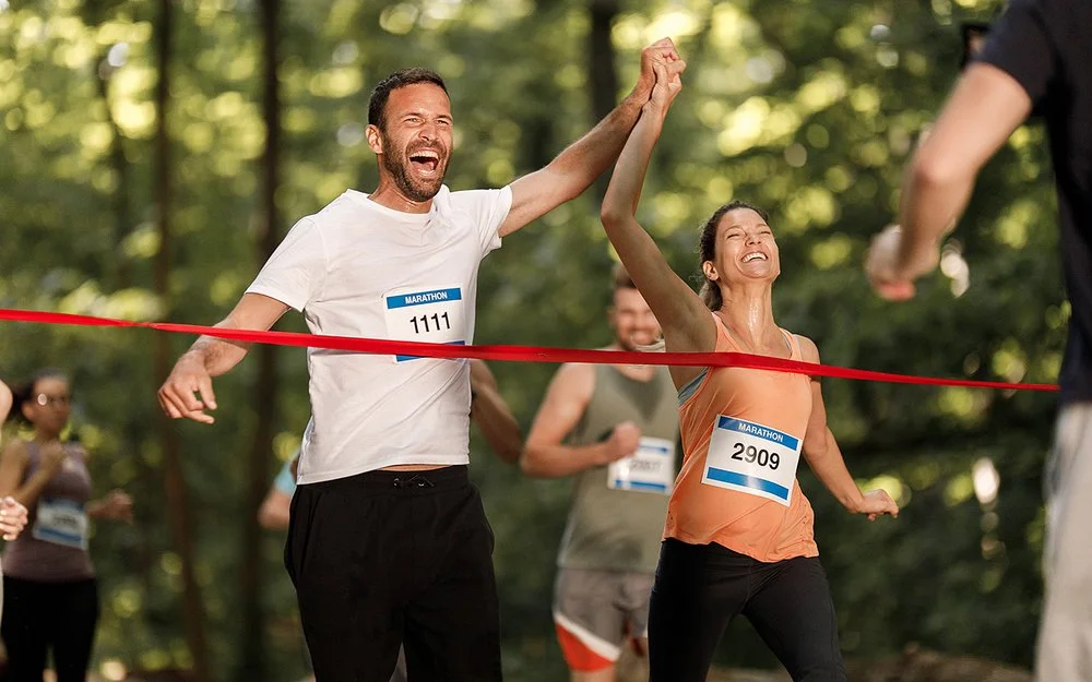 Ein junges Paar jubelt gemeinsam, während es das Band am Ziel eines Marathon-Laufs erreicht.