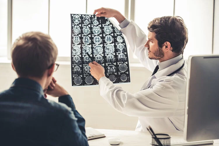 Neurologe bespricht Röntgenaufnahmen mit einem Patienten.