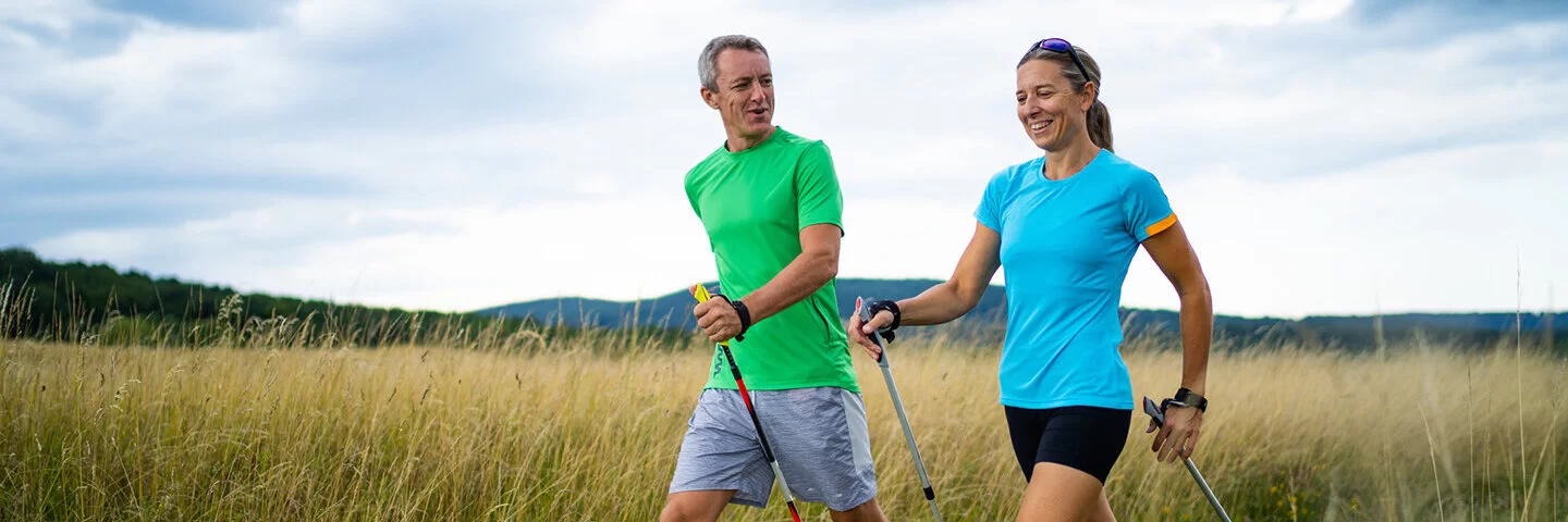 Ein Paar in sportlicher Kleidung betreibt gemeinsam Nordic Walking.