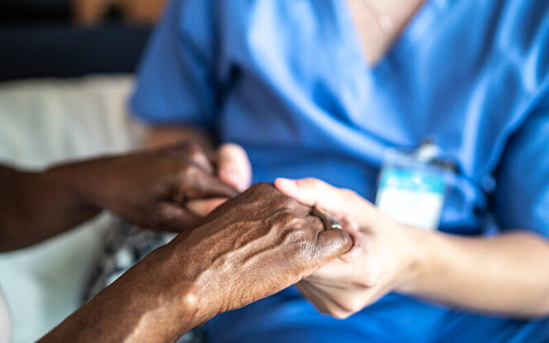 Eine Pflegerin hält die Hand einer demenzkranken Frau.