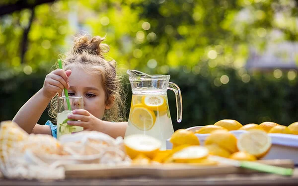 Kleines Mädchen steckt einen Trinkhalm in ein Glas mit selbstgemachter Limonade.