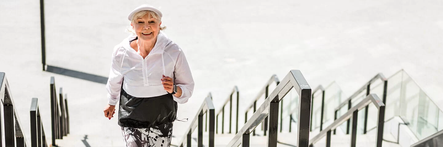 Eine fitte Seniorin in schwarz-weißem Sportdress joggt Treppenstufen hinauf.
