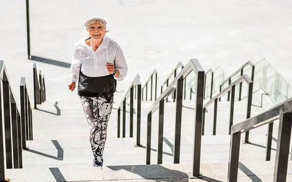 Eine fitte Seniorin in schwarz-weißem Sportdress joggt Treppenstufen hinauf.