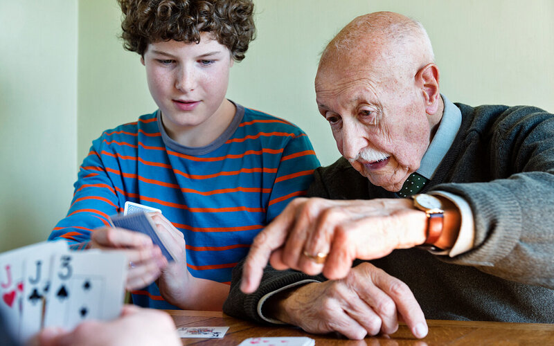 Opa mit Altersschwäche und Enkel spielen zusammen Karten.