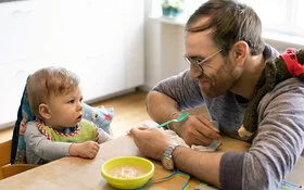 Ein Vater füttert sein Kind mit dem ersten Babybrei.
