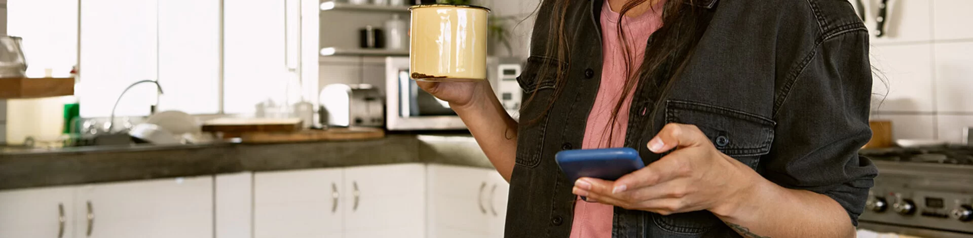 Frau steht in Küche und schaut auf Smartphone, sie exportiert ihre Daten aus der AOK Mein Leben-App.