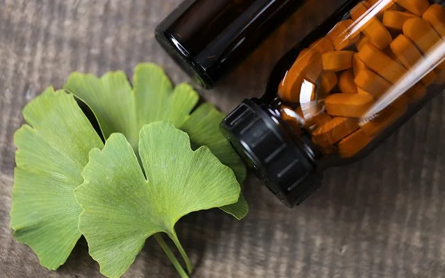 Ein Ginkgo-biloba-Blatt sowien ein braunes Fläschchen mit Tabletten liegen auf einem Tisch.