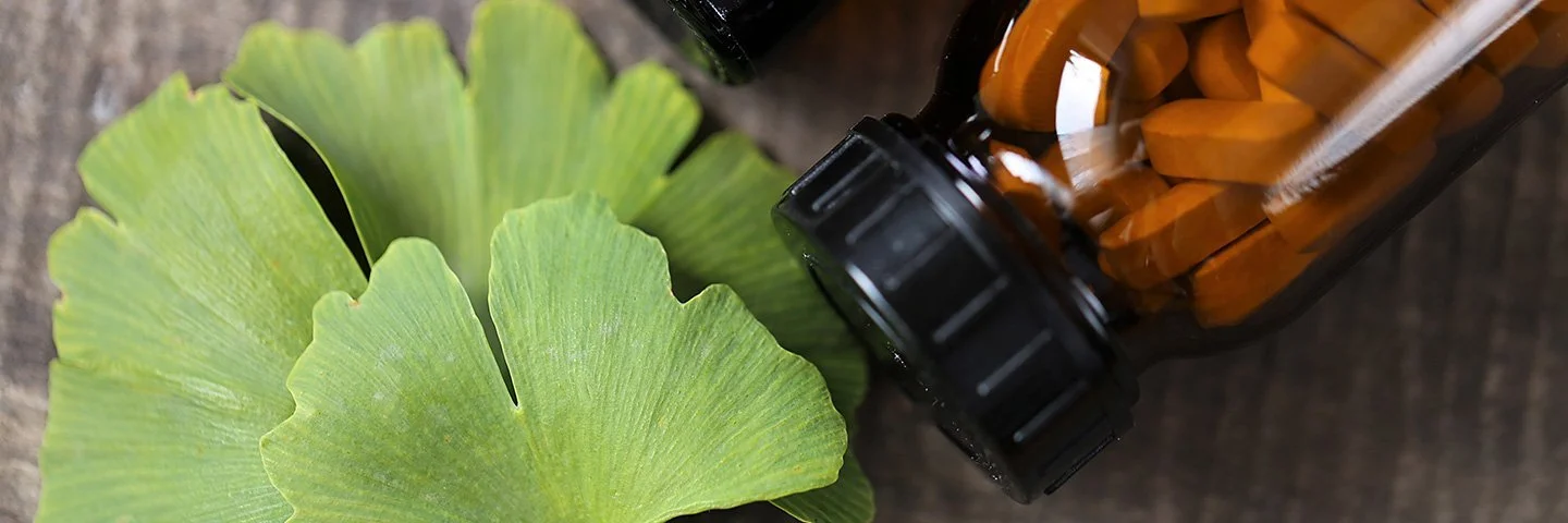 Ein Ginkgo-biloba-Blatt sowien ein braunes Fläschchen mit Tabletten liegen auf einem Tisch.