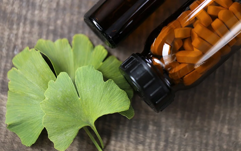 Ein Ginkgo-biloba-Blatt sowien ein braunes Fläschchen mit Tabletten liegen auf einem Tisch.