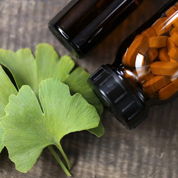Ein Ginkgo-biloba-Blatt sowien ein braunes Fläschchen mit Tabletten liegen auf einem Tisch.