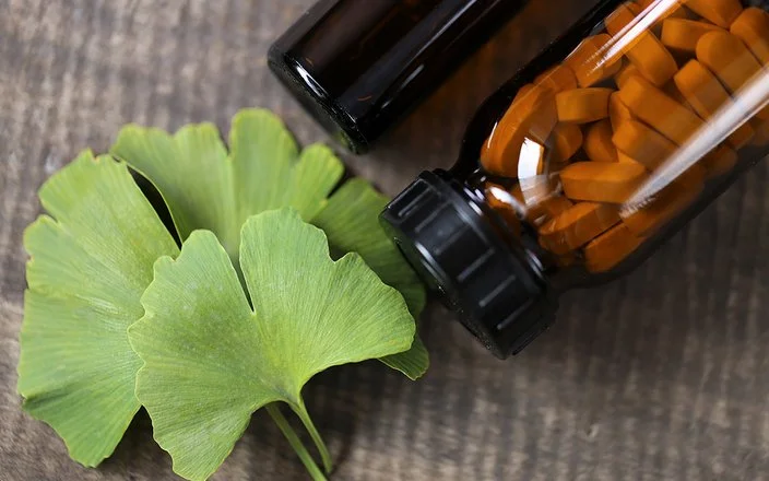 Ein Ginkgo-biloba-Blatt sowien ein braunes Fläschchen mit Tabletten liegen auf einem Tisch.
