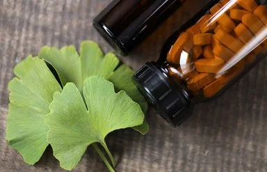 Ein Ginkgo-biloba-Blatt sowien ein braunes Fläschchen mit Tabletten liegen auf einem Tisch.