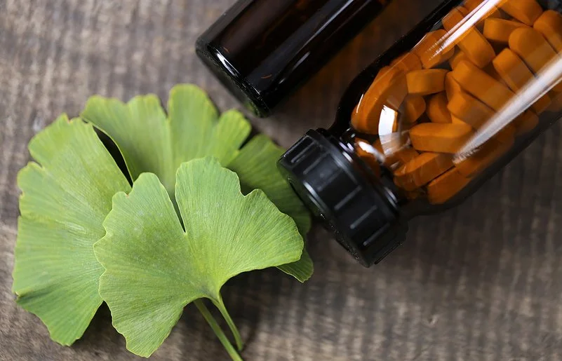 Ein Ginkgo-biloba-Blatt sowien ein braunes Fläschchen mit Tabletten liegen auf einem Tisch.