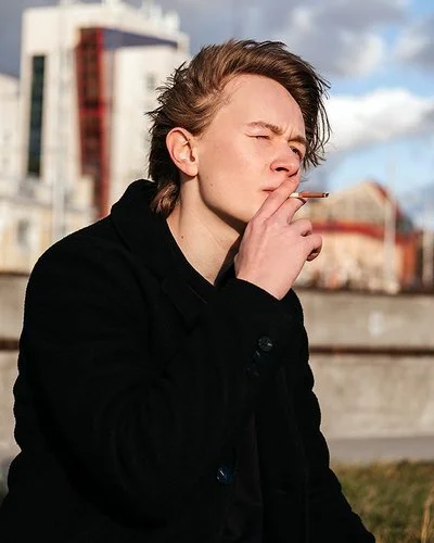 Ein Teenager sitzt vor der Skyline einer Stadt und raucht eine Zigarette.