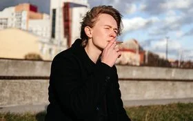 Ein Teenager sitzt vor der Skyline einer Stadt und raucht eine Zigarette.