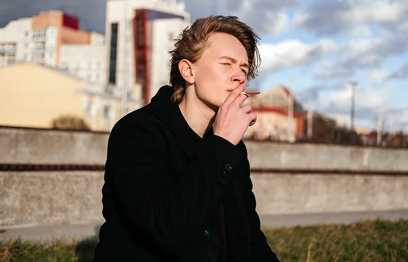 Ein Teenager sitzt vor der Skyline einer Stadt und raucht eine Zigarette.