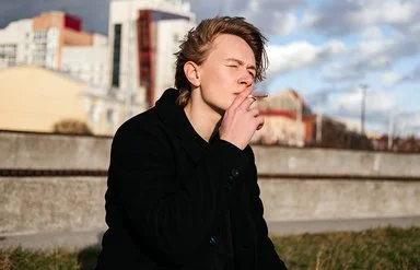 Ein Teenager sitzt vor der Skyline einer Stadt und raucht eine Zigarette.