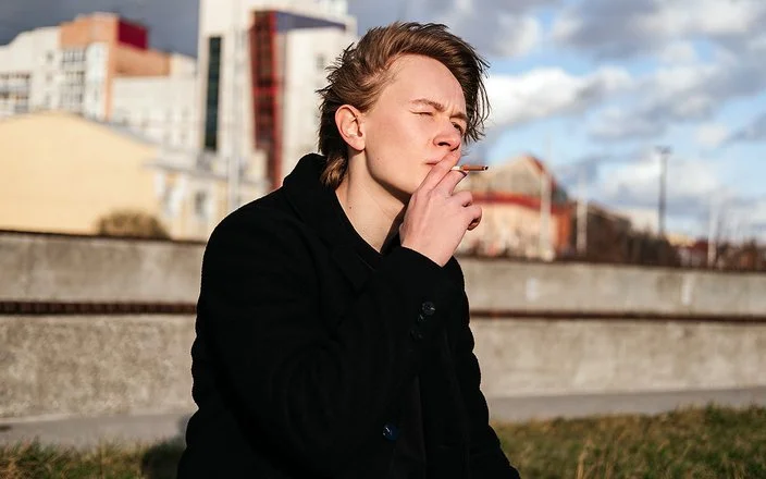 Ein Teenager sitzt vor der Skyline einer Stadt und raucht eine Zigarette.