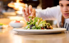 Eine junge Köchin in einem Restaurant dekoriert einen Salat, der auf einem Teller liegt.