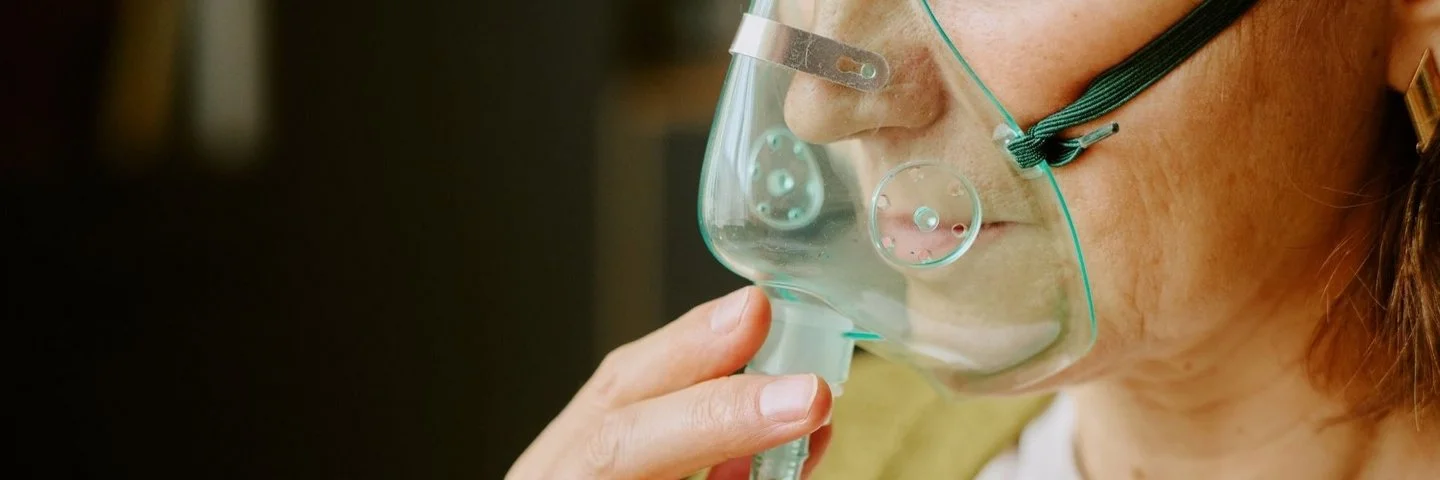 Eine Patientin hält sich eine Beatmungsmaske vor das Gesicht.