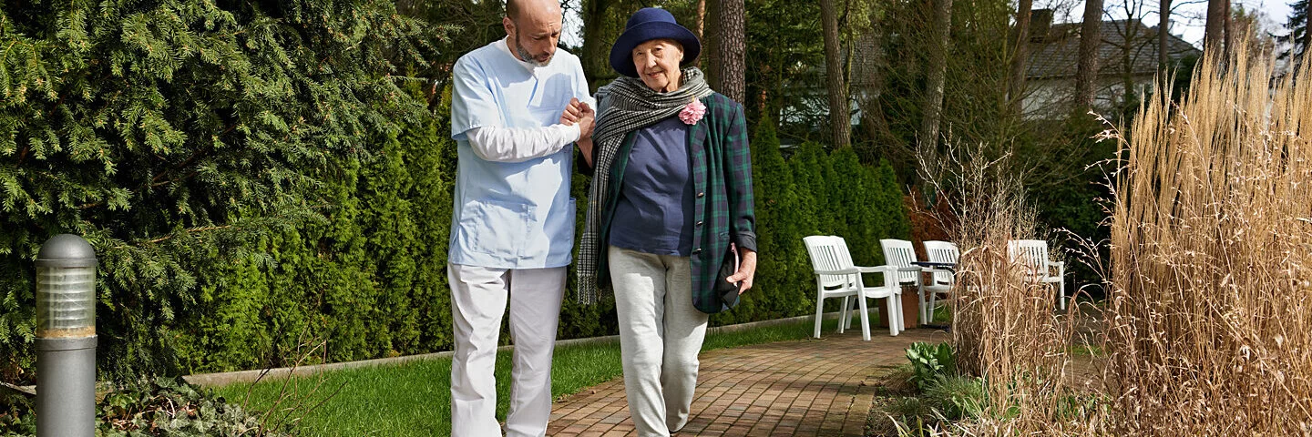 Eine ältere Frau geht mit einem Pfleger spazieren. Sie kann mit einer Betreuungsverfügung bestimmen, wer als rechtlicher Betreuer eingesetzt wird.