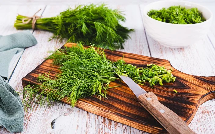 Frischer Dill liegt in einem Bündel auf dem Tisch, daneben geschnittener Dill in einer Schüssel.
