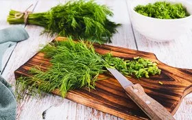 Frischer Dill liegt in einem Bündel auf dem Tisch, daneben geschnittener Dill in einer Schüssel.