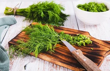 Frischer Dill liegt in einem Bündel auf dem Tisch, daneben geschnittener Dill in einer Schüssel.