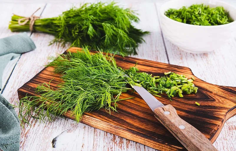 Frischer Dill liegt in einem Bündel auf dem Tisch, daneben geschnittener Dill in einer Schüssel.